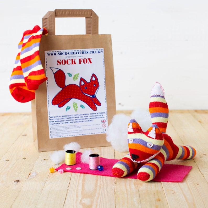 A Sock Fox craft kit - a paper bag with a picture of a jaunty fox, and a striped stuffed animal in front of it.